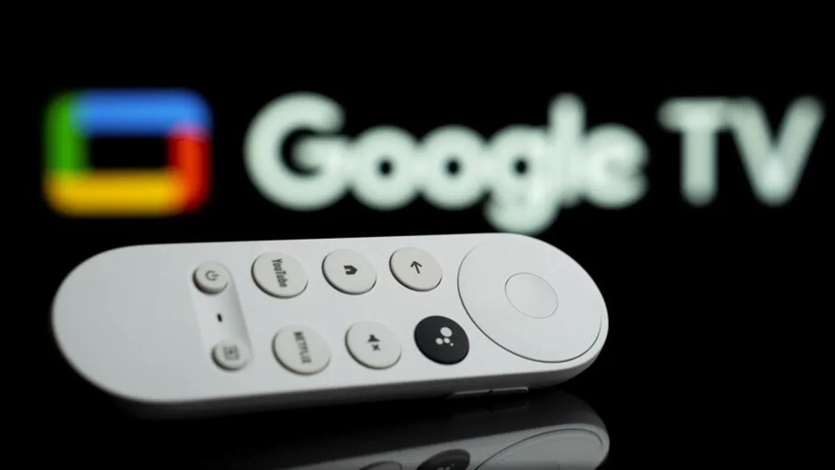 A close-up of a white Google TV remote, a key component of the Chromecast IPTV Australia setup, positioned in front of a blurred Google TV logo on a dark screen.